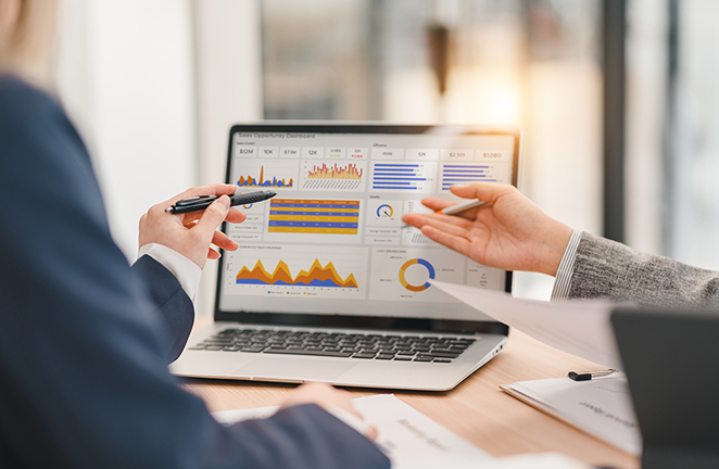Two professionals reviewing data and performance charts on a laptop during a meeting.
