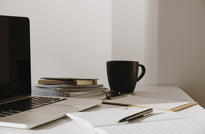 Minimal workspace with a laptop, notebooks, pen, and coffee mug on a desk.